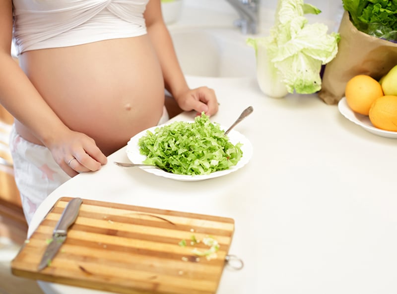 pregnant young woman mixing salad in a bowl